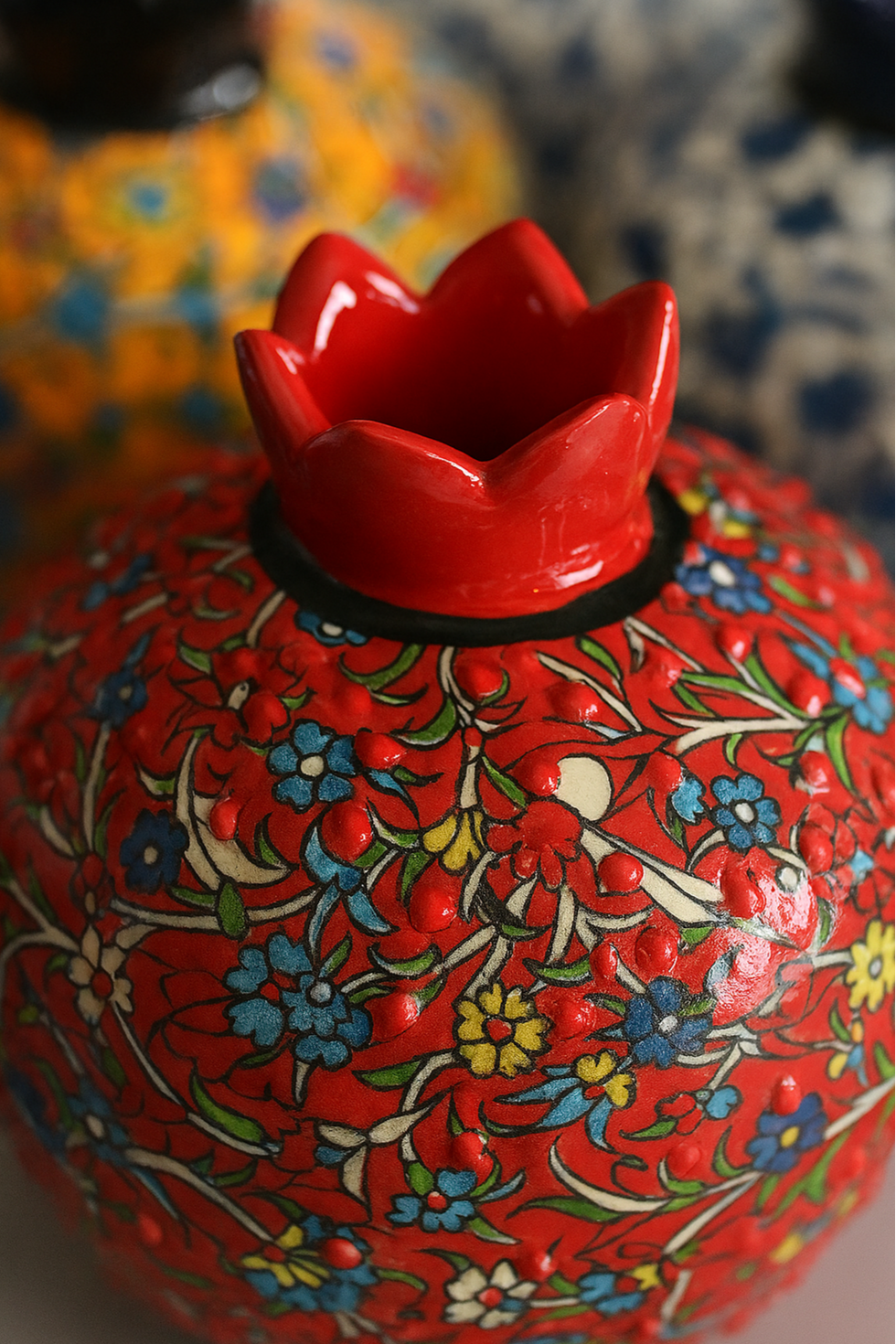 Decorative red vase with floral patterns and a red flower-shaped finial on a blurred background.